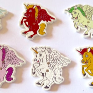 Op de afbeelding: Zes houten knopen in de vorm van gevleugelde eenhoorns. De eenhoorns zijn in verschillende kleuren, waaronder lichtblauw, rood, lichtgroen, roze, wit en geel.