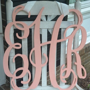 May include: A large, pink wooden monogram with the letters "HR" in a cursive script. The monogram is leaning against a white wooden rocking chair.