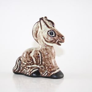 May include: A ceramic horse figurine in a seated position. The horse is primarily brown with white accents on the face and body. It has a black base and hooves, and a detailed mane and tail. The figurine is a decorative item.