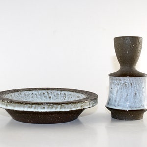 May include: A ceramic bowl and vase set. The bowl is round with a dark brown exterior and a white interior. The vase is a dark brown color on top and a light blue color on the bottom. The set has a speckled texture.