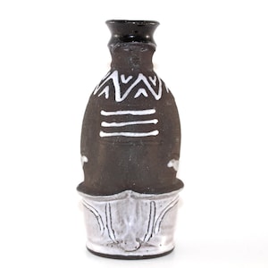 May include: A handcrafted ceramic vase with a black body and a white base. The vase features white geometric patterns and horizontal lines. The top of the vase is black. The vase is approximately 8 inches tall.