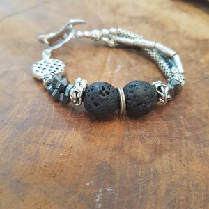 May include: A silver bracelet with black lava rock beads and silver accents. The bracelet has a clasp closure.