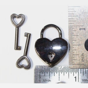 May include: A silver heart-shaped padlock with a key. The padlock is about 1 inch in size and is shown next to a ruler.