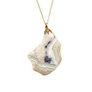 May include: A gold chain necklace with a pendant made of a large, irregularly shaped piece of agate. The agate is white with brown and gray banding.