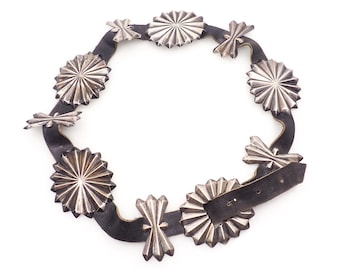 May include: A black leather belt with silver star-shaped embellishments. The belt has a buckle and is decorated with a repeating pattern of stars.