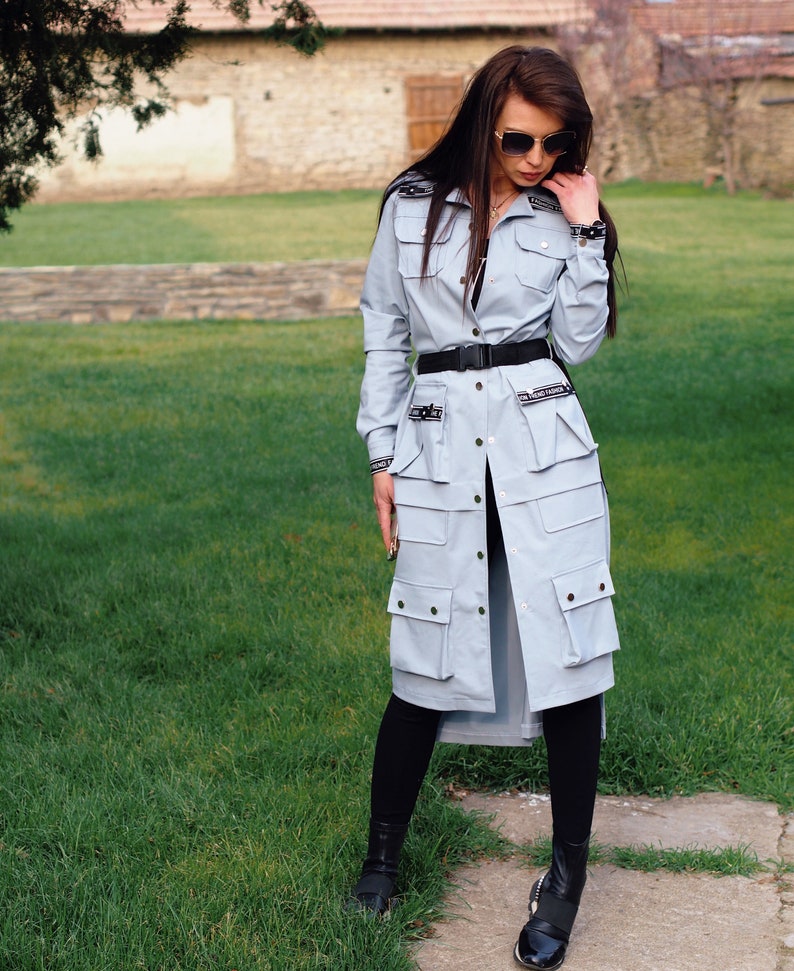 May include: A light blue long-sleeved shirt with a black belt and multiple pockets. The shirt has a button-down front and is worn with black leggings and black shoes.