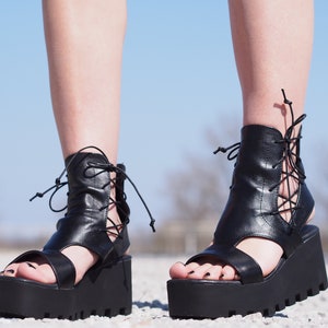 May include: Black leather platform sandals with lace-up detailing and a chunky platform sole.