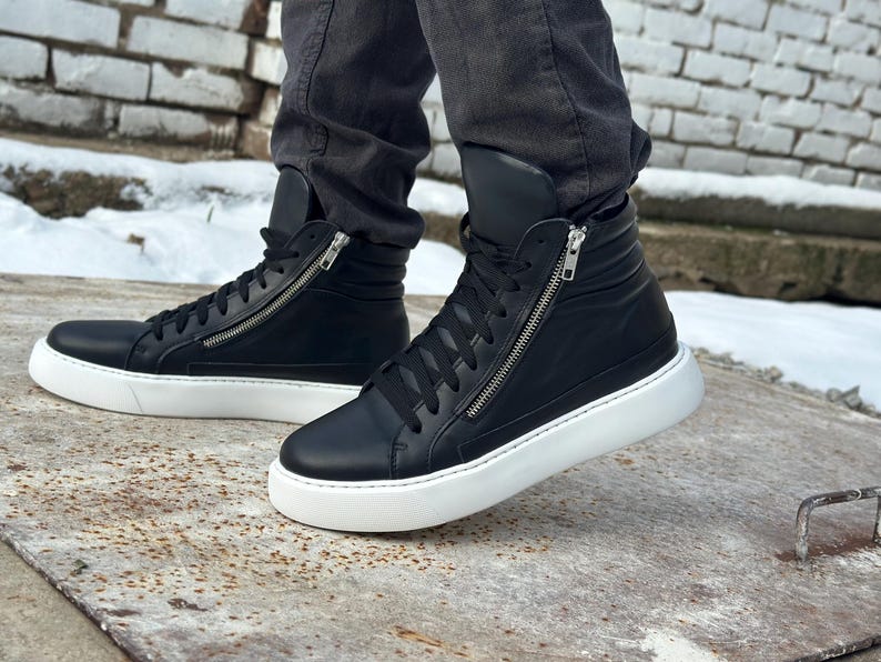 May include: Black leather high-top trainers with white soles and a zip detail on the side.