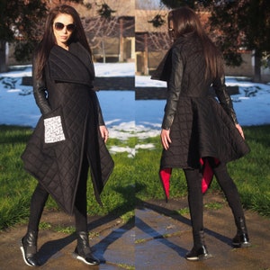 May include: A black quilted coat with a long, asymmetrical hemline. The coat has a large collar and long sleeves with leather accents. The coat has a pocket on the left side with a white patch that has handwritten text.