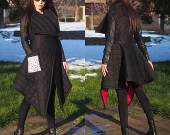 May include: A black quilted coat with a long, asymmetrical hemline. The coat has a large collar and long sleeves with leather accents. The coat has a pocket on the left side with a white patch that has handwritten text.