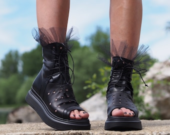 May include: Black leather platform sandals with lace-up detailing and a peep toe. The sandals have a chunky platform sole and are adorned with black tulle at the ankle.