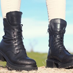 K&ouml;nnte beinhalten: Schwarze Lederstiefel mit Schn&uuml;rung, einem dicken Absatz und einem Rei&szlig;verschluss an der Seite.