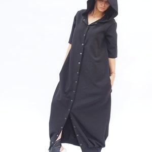 Puede incluir: Un vestido largo negro con capucha, con botones en la parte delantera y una falda larga y fluida.