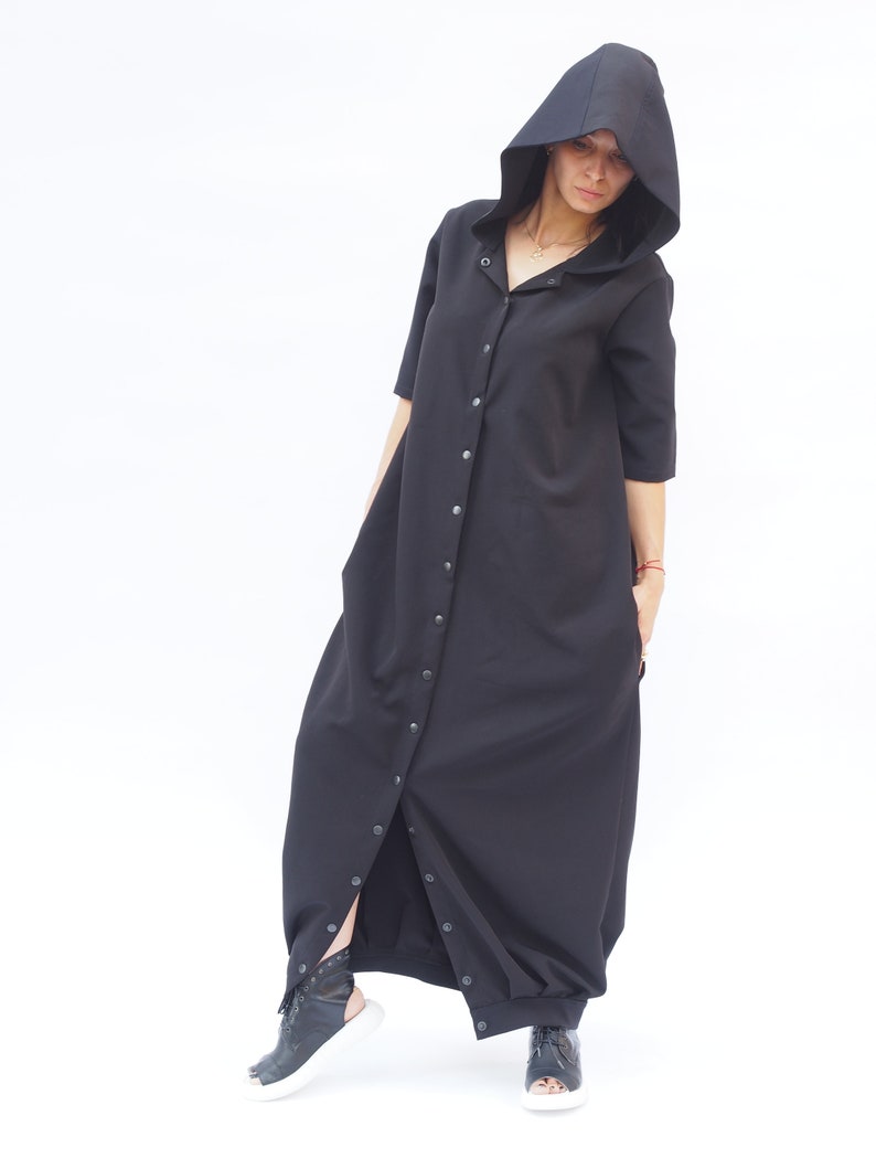 Puede incluir: Un vestido largo negro con capucha, con botones en la parte delantera y una falda larga y fluida.