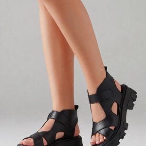 Pu&ograve; includere: Sandali neri con plateau e dettagli traforati. Questi sandali presentano una suola spessa e pi&ugrave; cinturini sul piede e sulla caviglia. I sandali sono realizzati in un materiale nero liscio e solido, che offre un look audace e moderno.