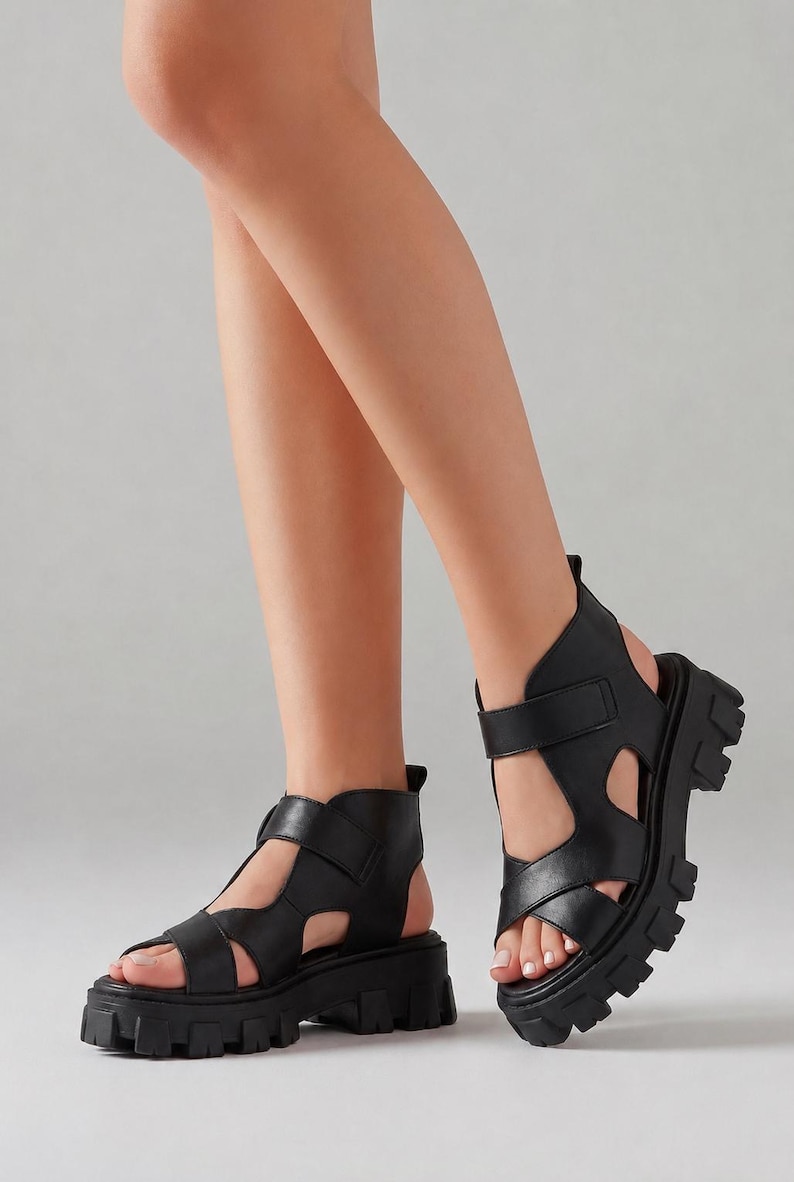 Pu&ograve; includere: Sandali neri con plateau e dettagli traforati. Questi sandali presentano una suola spessa e pi&ugrave; cinturini sul piede e sulla caviglia. I sandali sono realizzati in un materiale nero liscio e solido, che offre un look audace e moderno.