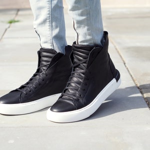May include: Black high-top sneakers with white soles. The sneakers have a zipper on the side and a quilted design on the back.