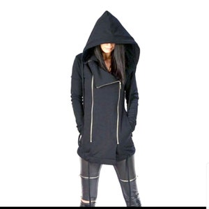 Könnte beinhalten: Schwarzer Kapuzenpullover mit Reißverschluss vorne und langem, asymmetrischem Saum. Der Pullover hat eine lockere Passform und einen lässigen Stil.