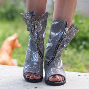 Op de afbeelding: Een paar zilveren glitter open-toe sandalen met ritsaccenten.