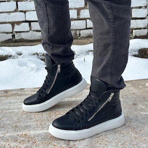 May include: Black leather high-top trainers with white soles and a zip detail on the side. The trainers have a lace-up closure and a padded collar.