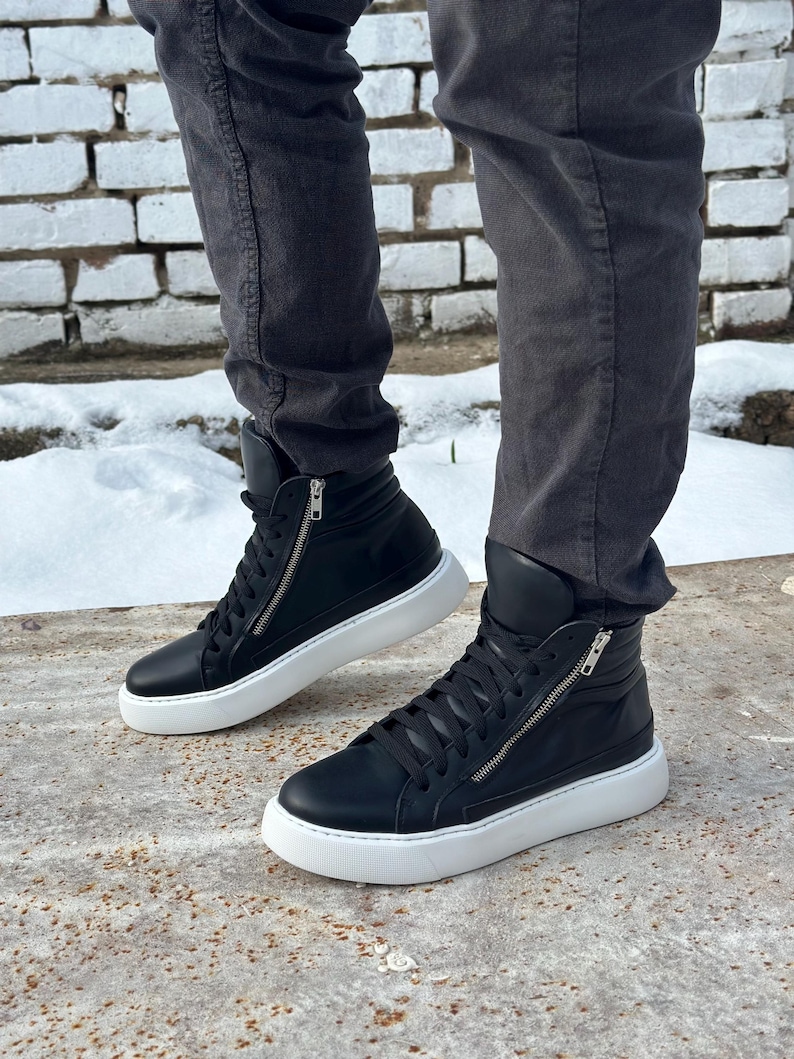 May include: Black leather high-top trainers with white soles and a zip detail on the side. The trainers have a lace-up closure and a padded collar.