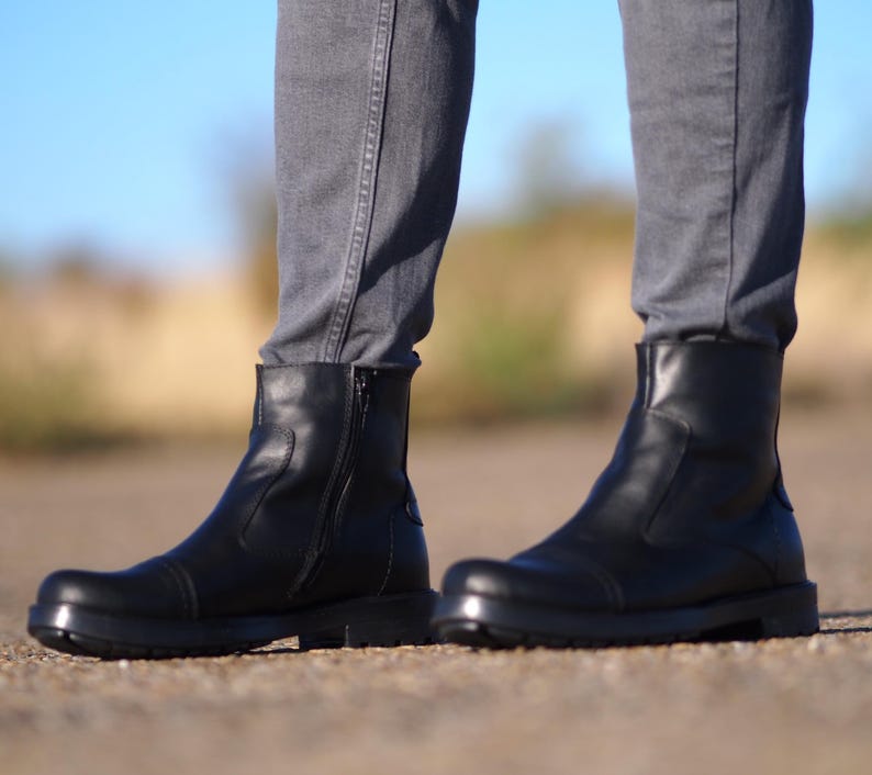 May include: Black leather ankle boots with a side zipper and a rounded toe. The boots have a thick sole and are worn with gray jeans. The boots are a classic style, suitable for various occasions.