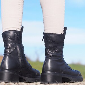 K&ouml;nnte beinhalten: Ein Paar schwarze Lederstiefel mit Rei&szlig;verschluss und Schn&uuml;rsenkeln. Die Stiefel haben ein Schlangenhautmuster an der R&uuml;ckseite des Kn&ouml;chels.