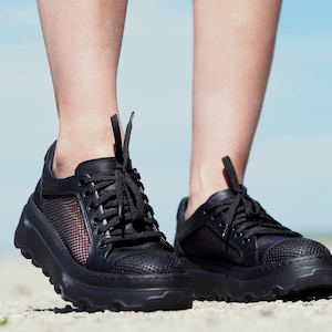 May include: Black sneakers with a mesh panel and a chunky sole. The sneakers have a lace-up closure.