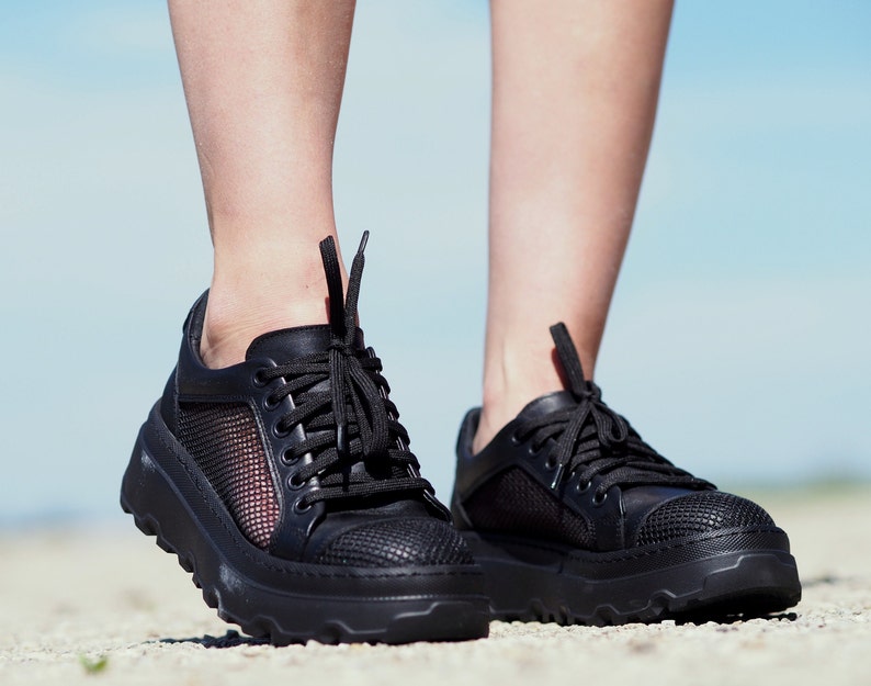 May include: Black sneakers with a mesh panel and a chunky sole. The sneakers have a lace-up closure.