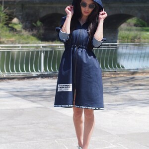 May include: A dark blue denim jacket with a hood and a zipper closure. The jacket has a drawstring waist and white text on the bottom hem and a patch on the front that says "If it's not yourself in your working wardrobe".