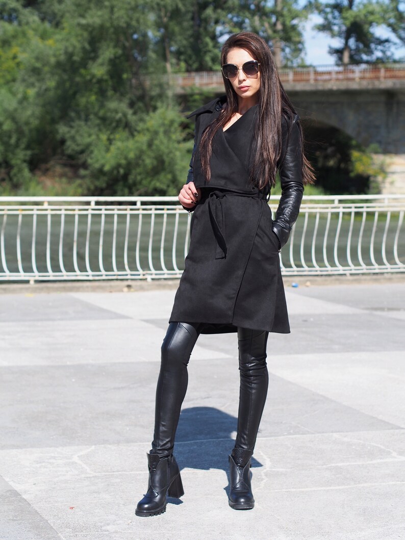 May include: A black long-sleeved coat with a wrap style and a belt. The coat has leather sleeves and is worn with black leggings and black ankle boots.