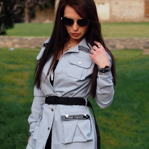 May include: A light blue long-sleeved jacket with a black belt and two pockets. The jacket has black text that says "Fashion Frend Fashion" on the front and back.