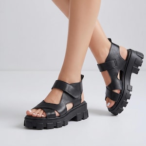 Pu&ograve; includere: Sandali in pelle nera con suola spessa e carrarmato. I sandali hanno cinturini regolabili. Il design a punta aperta e la suola spessa offrono un look moderno. I sandali sono un'opzione di calzatura elegante. La suola misura circa 5 cm.