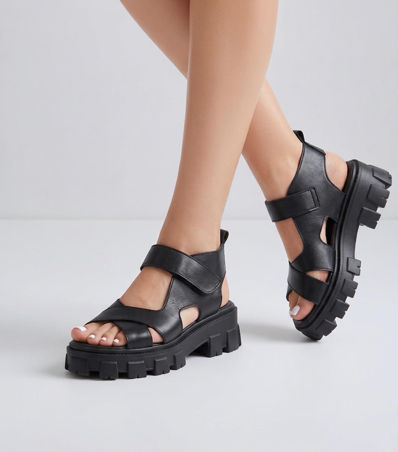 Pu&ograve; includere: Sandali in pelle nera con suola spessa e carrarmato. I sandali hanno cinturini regolabili. Il design a punta aperta e la suola spessa offrono un look moderno. I sandali sono un'opzione di calzatura elegante. La suola misura circa 5 cm.
