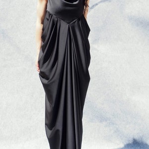 May include: A black sleeveless maxi dress with a cowl neck and a draped design. The dress is made of a soft, flowing fabric.