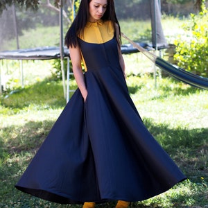 May include: A woman wearing a navy blue dress with a yellow collar and a full skirt. She is standing in a grassy area.