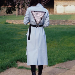 May include: A light blue long-sleeved shirt with a black belt and a triangular print on the back. The print features the text "By Mackay on Great Fights".