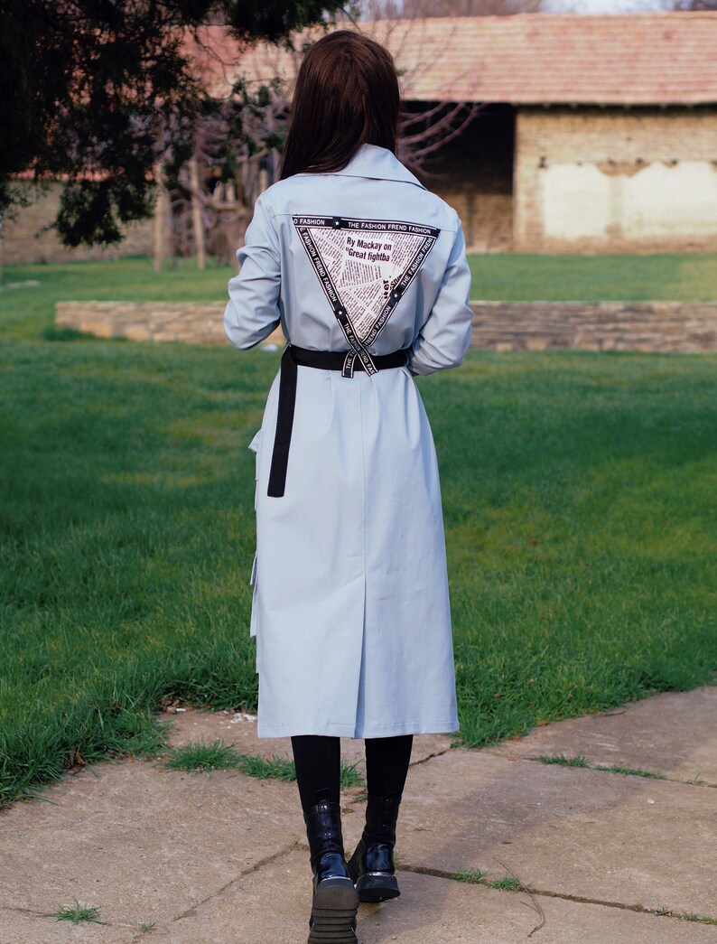 May include: A light blue long-sleeved shirt with a black belt and a triangular print on the back. The print features the text "By Mackay on Great Fights".
