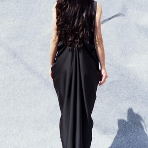May include: A woman wearing a long black dress with a flowing, draped back. The dress is sleeveless and has a simple, elegant design.