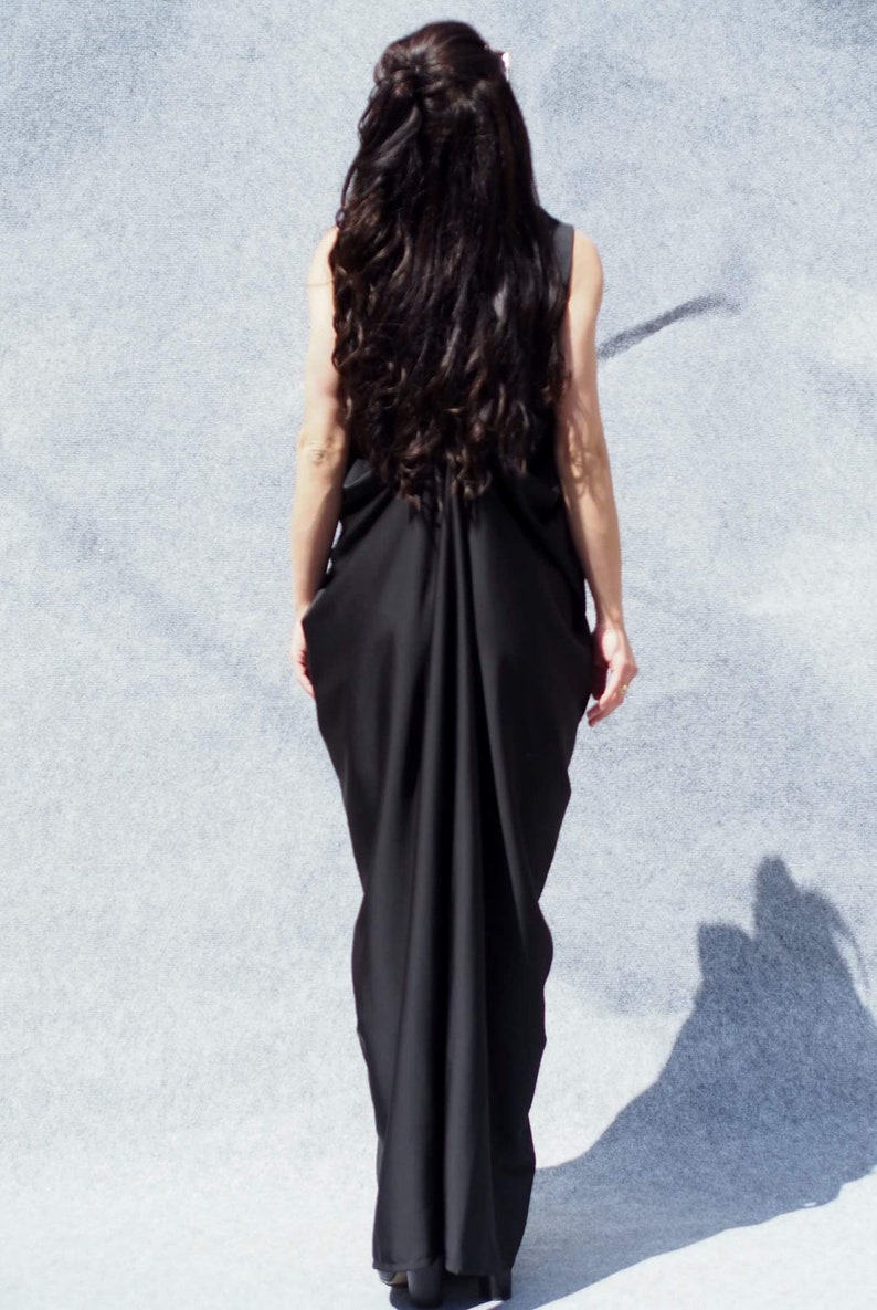 May include: A woman wearing a long black dress with a flowing, draped back. The dress is sleeveless and has a simple, elegant design.