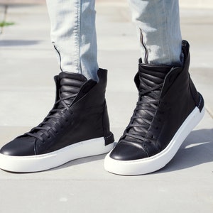 May include: Black high-top sneakers with white soles. The sneakers are made of leather and have a lace-up closure.