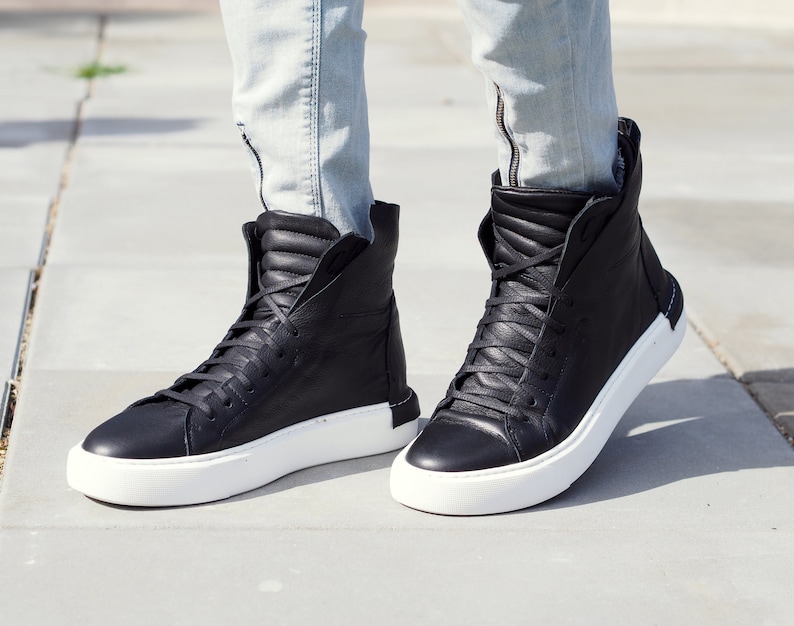 May include: Black high-top sneakers with white soles. The sneakers are made of leather and have a lace-up closure.