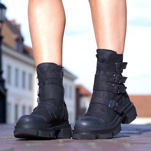 May include: Black ankle boots with a chunky sole and multiple buckle straps. The boots have a rugged, edgy design, perfect for adding a bold statement to any outfit. The boots are made of a durable material and feature a zipper closure.