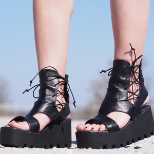 May include: Black leather platform sandals with lace-up detailing on the ankle and a thick platform sole.
