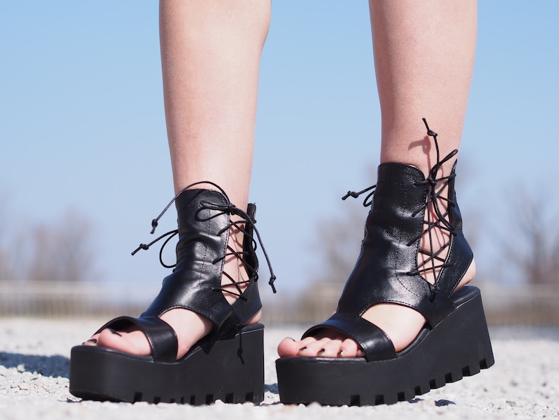 May include: Black leather platform sandals with lace-up detailing on the ankle and a thick platform sole.