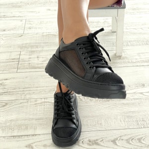 May include: Black platform sneakers with mesh panels and black laces. The sneakers have a chunky sole.