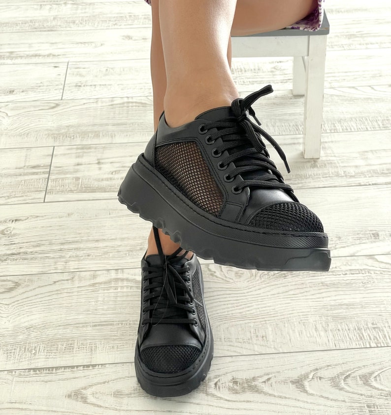 May include: Black platform sneakers with mesh panels and black laces. The sneakers have a chunky sole.