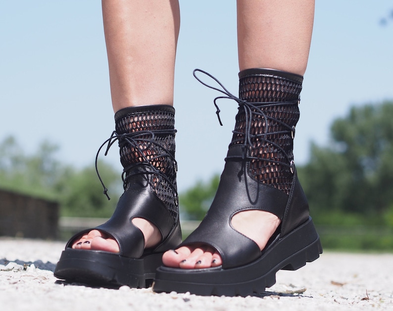 May include: Black leather sandals with a mesh upper and lace-up closure. The sandals have a thick platform sole and a chunky heel.
