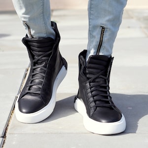 May include: Black high-top sneakers with white soles. The sneakers have a lace-up closure and a padded collar.