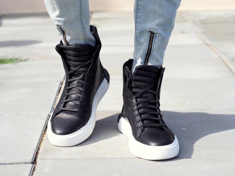 May include: Black high-top sneakers with white soles. The sneakers have a lace-up closure and a padded collar.